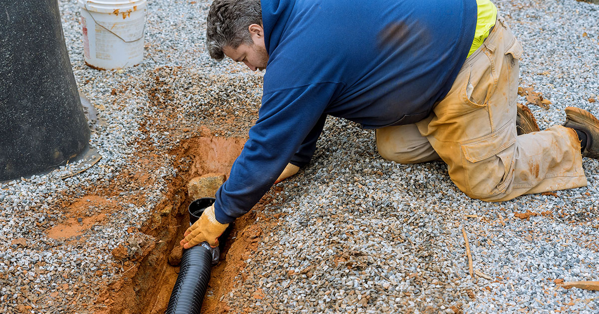 A person installing a French drain without a fabric liner, one of the most common French drain mistakes.