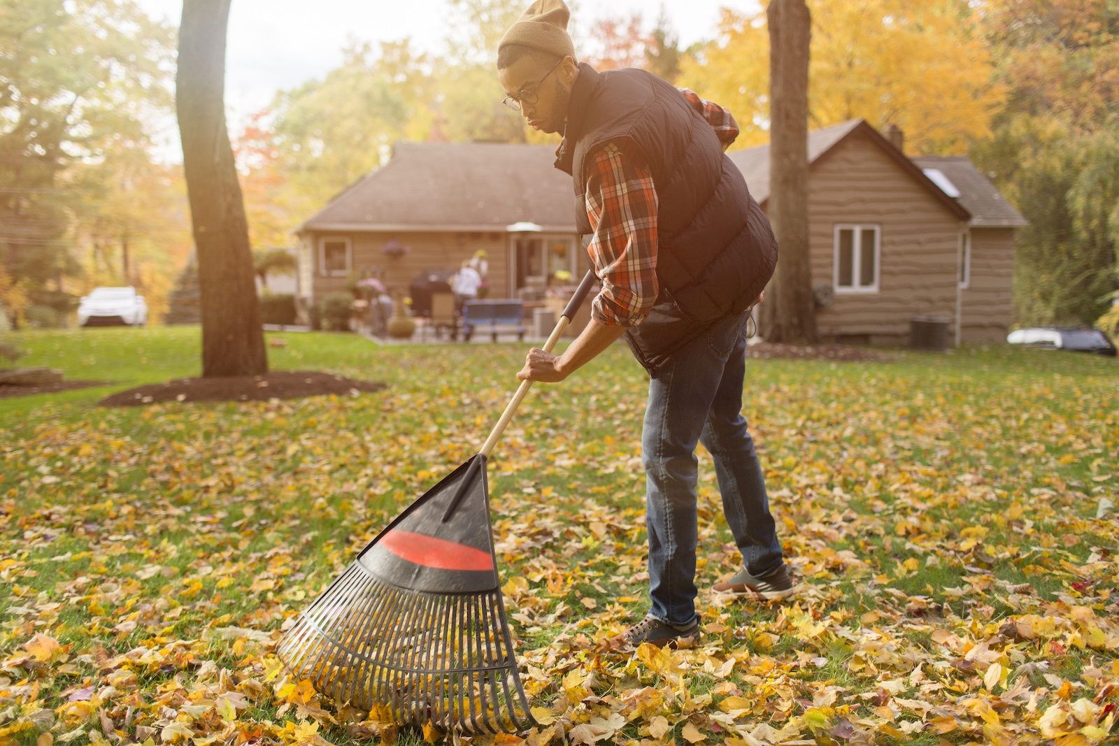 A young man raking the leaves on his lawn, part of his yard care in the fall routine.
