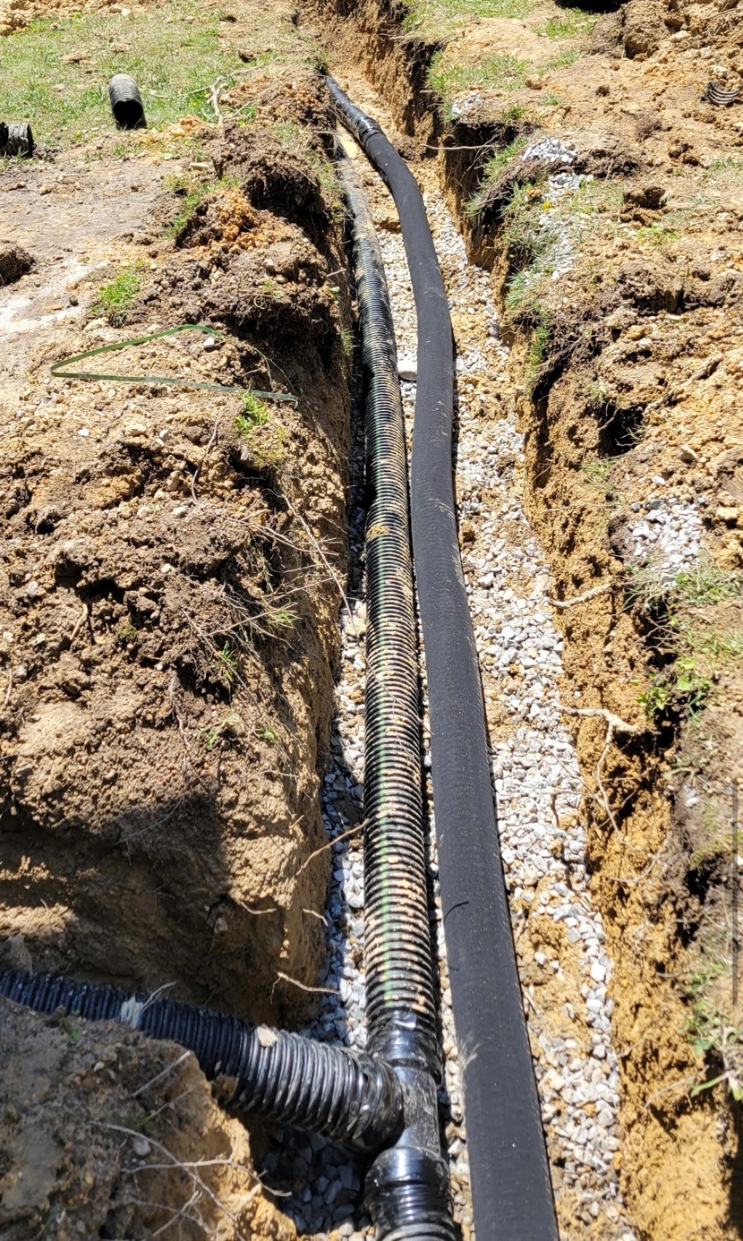 Perforated French drain pipe alongside solid conduit pipe laid on a gravel bed inside an excavated trench in Ooltewah TN