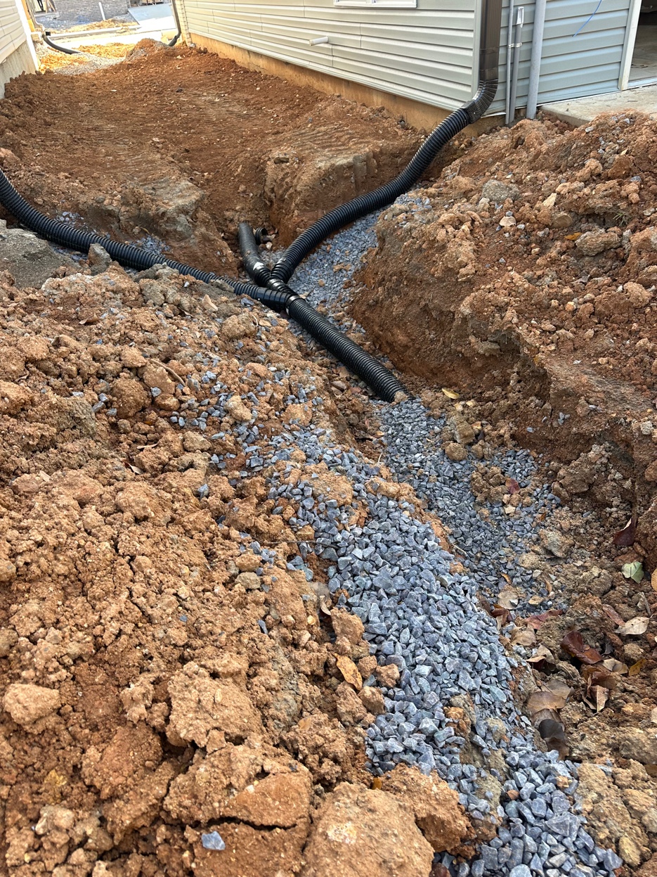 Black corrugated drainage pipes connected at a junction point bedded in number 57 drainage gravel during French drain installation